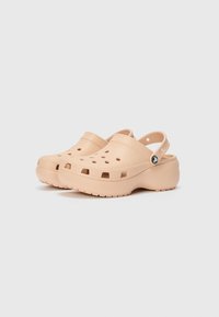 Peach-colored clogs with a perforated upper, adjustable back strap, and textured sole. Made of lightweight, durable material.
