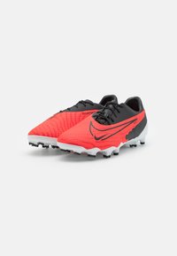 Botas de fútbol Nike Phantom con una parte superior texturizada en rojo, detalles en negro y una suela blanca que presenta tacos multidireccionales para mayor tracción.