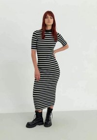 Zwart-wit gestreepte midi-jurk met een aansluitende silhouet, korte mouwen en ronde halslijn, gecombineerd met zwarte veterschoenen met platform.