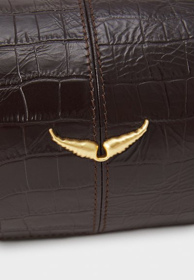 Hnedá kožená kabelka s reliéfom krokodíla, vybavená zlatým emblémom s krídlami a kontrastným hnedým prešívaním. Textúrovaný povrch s viditeľnými vzormi.