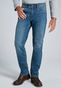 Jeans de color azul claro con un diseño de pierna recta, con un desgaste sutil y efecto de arrugado, estilo de cinco bolsillos, combinados con zapatos de cuero marrón.
