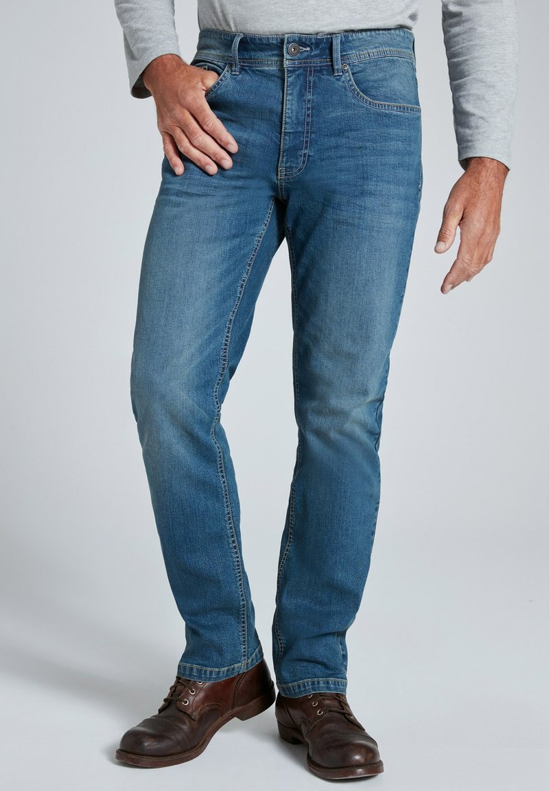 Jeans de color azul claro con un diseño de pierna recta, con un desgaste sutil y efecto de arrugado, estilo de cinco bolsillos, combinados con zapatos de cuero marrón.