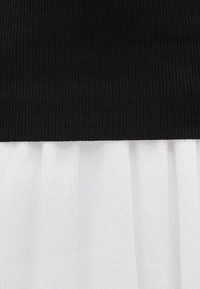 Top negru cu dungi, cu o secțiune inferioară plisată albă, având țesături texturate și culori contrastante, creând un design bicolor.