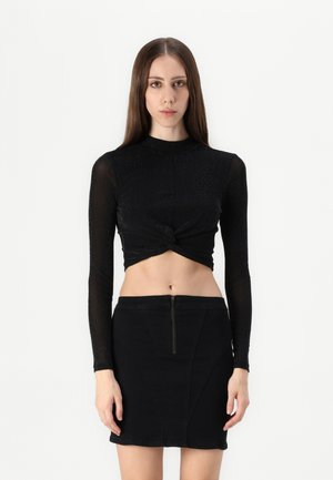 Black long-sleeve crop top with a twisted front design, made of textured fabric. Paired with a black mini skirt featuring a front zipper.