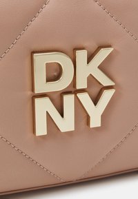 Cuir matelassé beige avec lettres métalliques dorées formant DKNY, détails de couture visibles sur la surface du cuir.