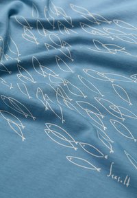 Tela azul con un patrón repetido de peces blancos. La textura es suave, resaltando la simplicidad juguetona y la ligereza del diseño.
