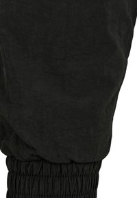 Svarta byxor med en skrynklig textur, rynkad elastisk midja och avsmalnande ben. Tyget verkar lätt och matt.