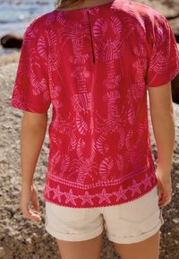 Haut rouge à manches courtes avec un motif de homard et des accents d'étoiles de mer à l'ourlet. Texture lisse avec un léger éclat, comprenant un détail œillet dans le dos.