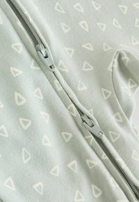 Ljusgrön zip-up-plagg med en mjuk textur, som har ett upprepat mönster av ljusgrädde trianglar. Dragkedja i matchande färg.
