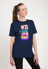 Námořnická modrá tričko s živými, vícebarevnými texty ve stylu graffiti: "NYC," "Paříž," "Londýn." Krátké rukávy, volný střih, bavlněný materiál.