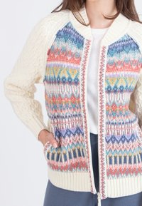Cárdigan de punto con cuerpo crema, patrones fair isle coloridos en naranja, azul y verde, y mangas de punto trenzado texturizado. Con cremallera frontal y bolsillos.