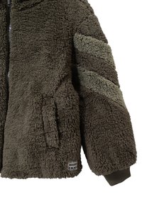 Chaqueta de forro polar en color verde olivo oscuro con una superficie texturizada y esponjosa, que cuenta con cremallera frontal, bolsillo lateral y rayas verdes en las mangas.