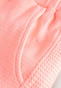 Tissu rose clair présentant une surface texturée avec de petits points en relief. Texture douce avec une taille froncée et des bords lisses.