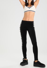 Svarta sammetstights med sidränder i detaljer, matchat med en vit och marinblå sportbh. Slank, kroppsnära design. Svarta plattformssneakers.