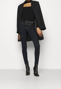 Svart polotröja, mörkblå slim fit-jeans och en svart midjeväska. En lång svart kappa och svarta ankelboots fulländar outfiten. Släta texturer.