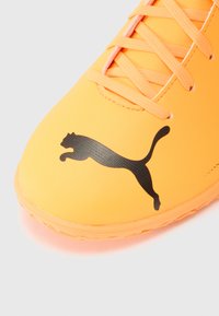 Zapatilla deportiva de color amarillo brillante con superficie texturizada, que presenta el logo de Puma en negro y cordones naranjas a juego. Suela lisa para mayor tracción.