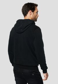 Must kapuutsiga dressipluus pehme tekstuuriga, millel on kängurutasku ja soonikkoes mansetid. Lihtne disain ilma nähtavate mustrite või logodeta.