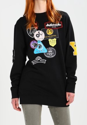 Sudadera negra con parches coloridos de temas de viaje, que incluyen diseños de "Atenas", "Palace Hotel Vegas", "King George Londres" y "Royal Boat".