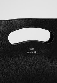 Sac en cuir noir texturé avec une poignée incurvée découpée et les mots "WON HUNDRED" embossés en blanc sous la poignée.
