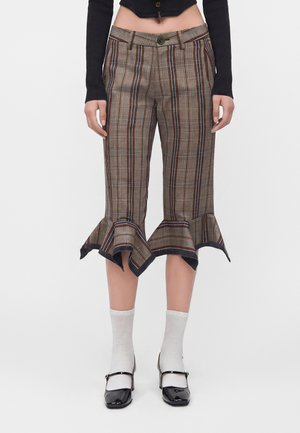 Pantalon court à carreaux avec ourlets évasés et volantés, porté avec des chaussettes blanches et des chaussures Mary Jane noires, assorti à un top court noir.