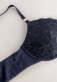 Tamsiai mėlyna liemenėl�ė su nėrinių sluoksniu ant kaušelių, lygiu audinio dirželiu, reguliuojamu dirželiu su auksinėmis detalėmis ir apvalia forma.