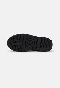 Suela de zapato de goma negra con un patrón texturizado. Presenta símbolos en relieve: una 'O', una línea diagonal y una forma estilizada de 'Y'.