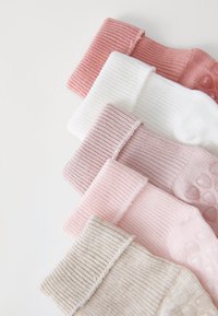 Calcetas acanaladas en tonos de rosa, blanco y beige. Con suelas texturizadas con patrones de corazones y bordes de puño en contraste. Material suave.