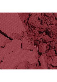 Poudre de maquillage rouge profond écrasée avec une surface pressée texturée en forme de grille sur certains fragments et de la poudre libre sur d'autres.