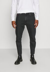 Svarta denimjeans med slim fit, med femficksdesign, metallknappstängning och subtil detalj i röd logotyp. Bärs med svarta ankelskålar.