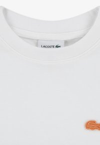 Λευκό βαμβακερό t-shirt με στρογγυλή λαιμόκοψη και μικρό πορτοκαλί λογότυπο κροκόδειλου της Lacoste κεντημένο στην αριστερή πλευρά.
