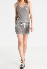 Mono corto gris de tirantes con un escote redondeado, estampado de palmeras, cintura con cordón y textura suave. Combinado con sandalias de dedo con estampado.