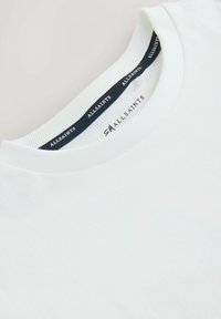 Bílý tričkový límec s černou visačkou AllSaints a potiskem velikosti "SM" uvnitř výstřihu.