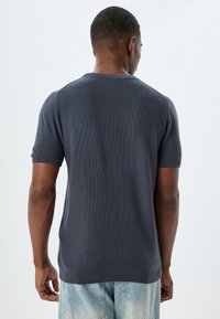 Marineblauwe kortemouw trui met een gestructureerd breisel, ronde halslijn en geribde manchetten. Draagt met lichtblauwe versleten spijkerjeans.