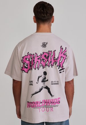 Person trägt ein hellbeiges T-Shirt mit pinken und schwarzen Grafiken einer laufenden Silhouette und fettem Text, darunter "Siksilk" und "Worldwide Tour."