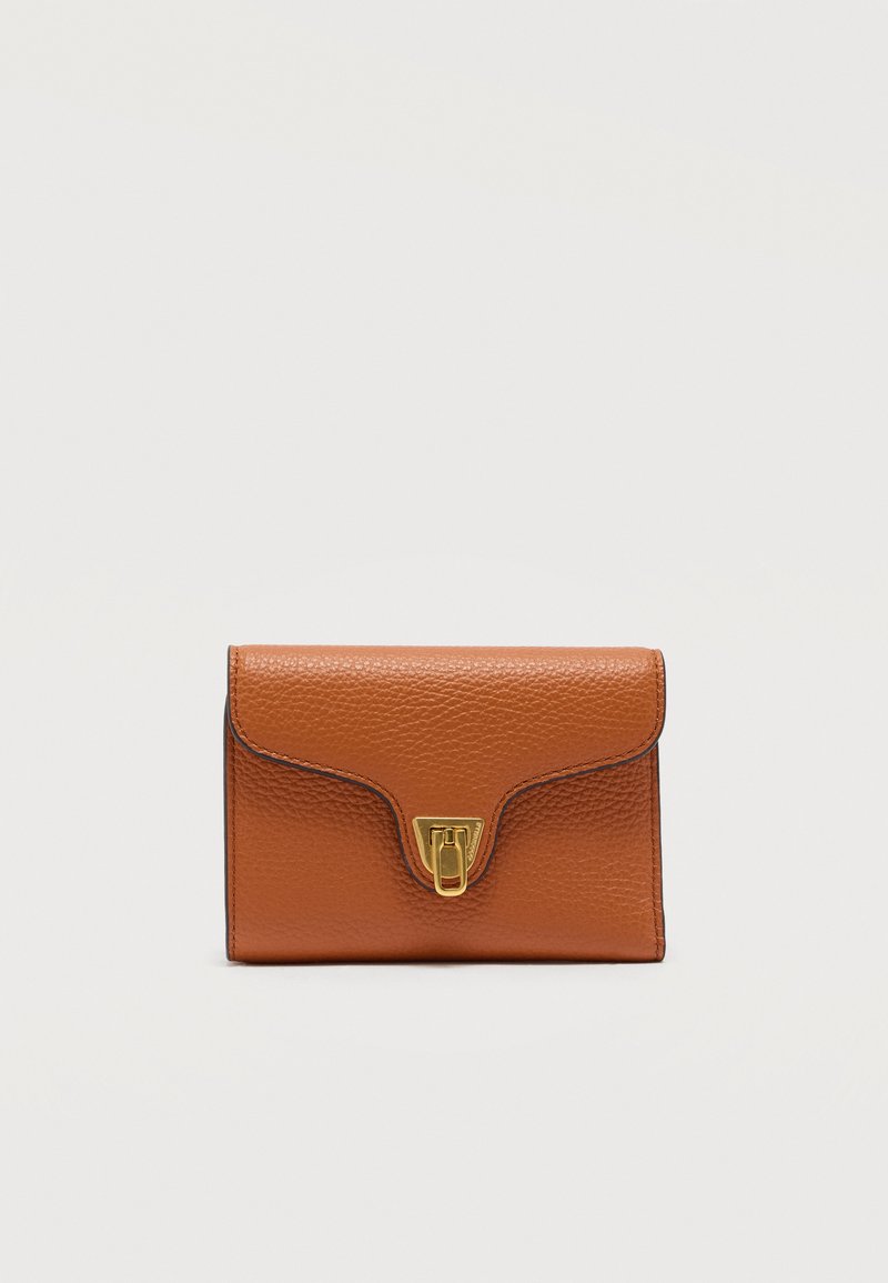 Μικρό καφέ δερμάτινο πορτοφόλι με υφή ψαμμίτη και κούμπωμα σε χρυσό τόνο, φωτογραφημένο πάνω σε απλό φωτεινό φόντο.