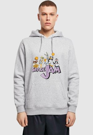 Jaunas vyras dėvi pilką džemperį su kapišonu, kuriame pavaizduoti „Space Jam“ personažai, laikantys krepšinio kamuolius, o priekyje parašyta „Space Jam“.