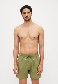 Shorts de bain vert olive en tissu léger, avec une taille élastique dotée d'un cordon de serrage ajustable et des poches latérales.