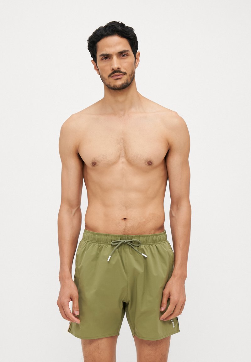 Shorts de bain vert olive en tissu léger, avec une taille élastique dotée d'un cordon de serrage ajustable et des poches latérales.