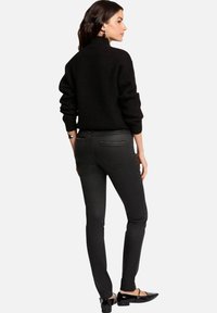 Suéter de punto negro con cuello alto, combinado con jeans skinny negros que tienen bolsillos traseros decorativos. Unos zapatos planos negros completan el atuendo.