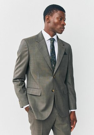 Graue karierte Anzugjacke mit zwei Knöpfen, Reverskragen und seitlichen Taschen. Getragen über einem weißen Hemd und einer gemusterten Krawatte.