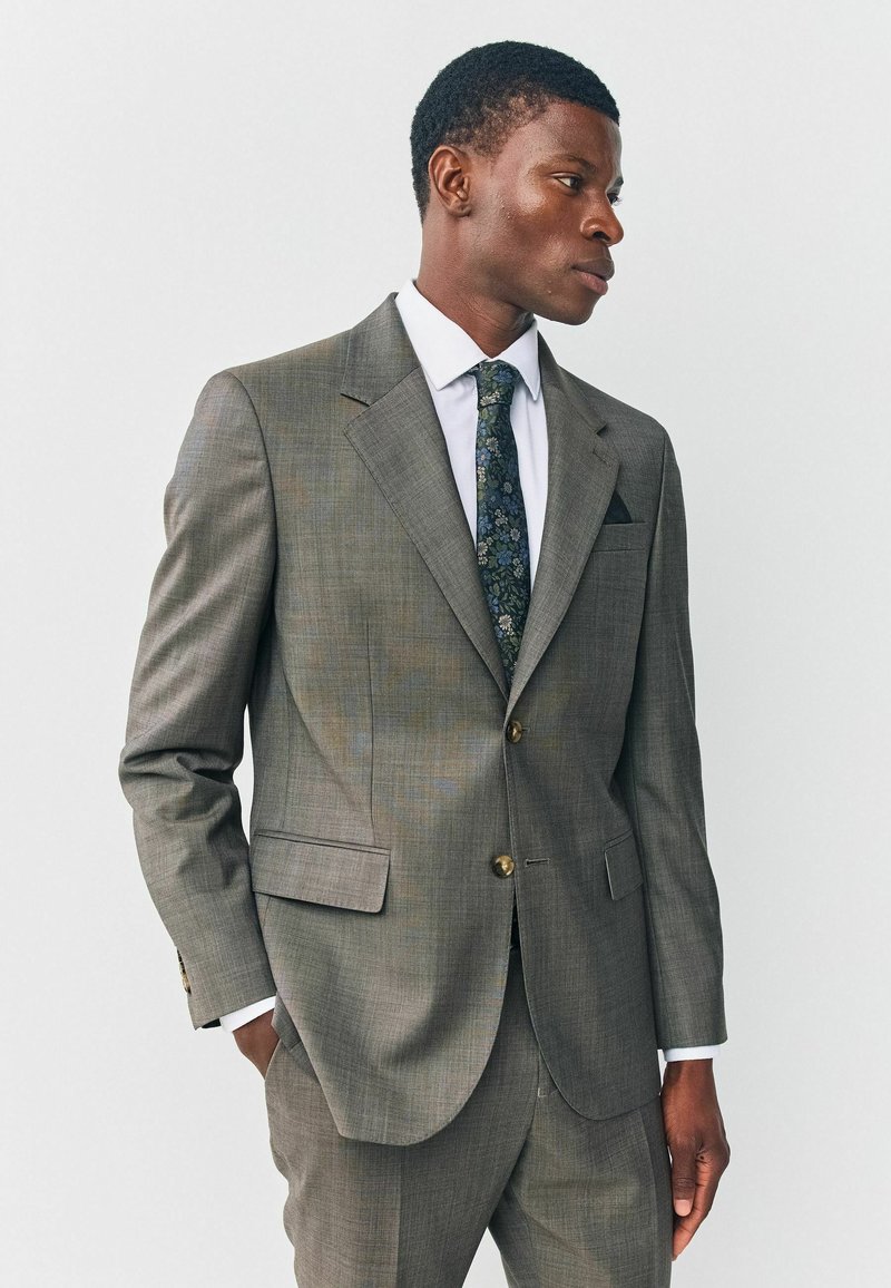 Graue karierte Anzugjacke mit zwei Knöpfen, Reverskragen und seitlichen Taschen. Getragen über einem weißen Hemd und einer gemusterten Krawatte.