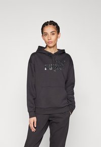 Sudadera negra hecha de un tejido suave, con un bolsillo canguro, puños acanalados y un logo brillante en el pecho.