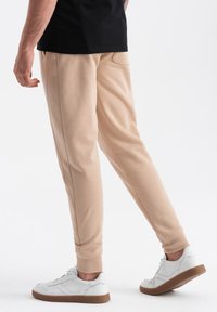 Beige sweatpant met een slim fit, taps toelopende benen en zijzakken, gecombineerd met witte sneakers met een bruine zool.