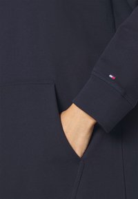 Felpa blu navy con tasca a marsupio, polsini a costine e un piccolo logo tricolore sulla manica. Texture morbida, design casual.