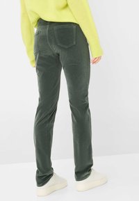 Mørkegrønne kordfløjspants med slim fit, fem-lomme design og subtil struktur, parret med en lys grå sko.