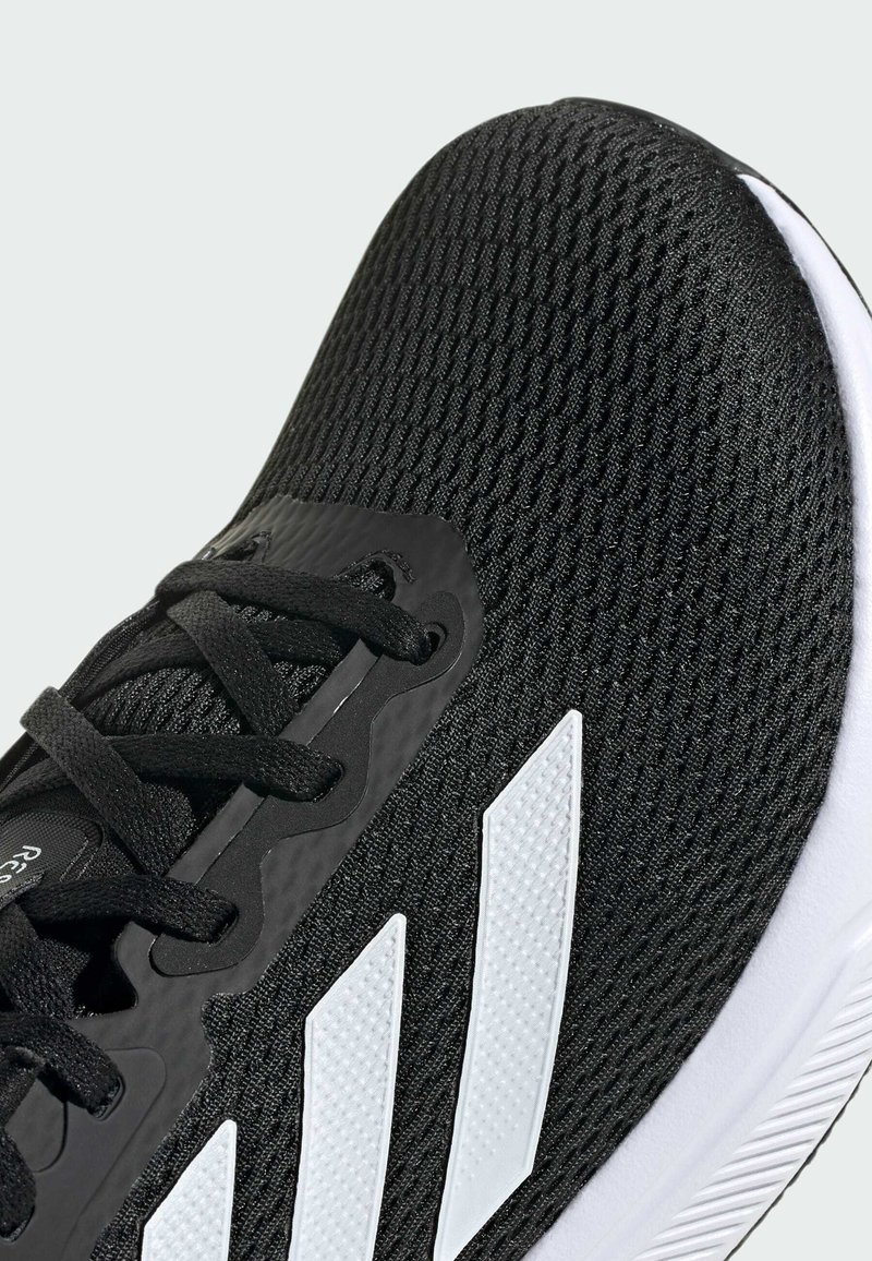 Zapatilla deportiva negra con una parte superior de malla texturizada, acentos de tres rayas en blanco y una suela de goma blanca. Presenta cordones negros y un diseño elegante.