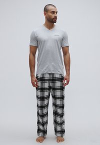 Grå v-hals t-shirt med "GUESS"-logo, kombineret med sort-hvide ternede flanellbukser. Behagelig pasform og blød tekstur, barfodet.