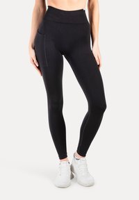 Hoge taille zwarte leggings van rekbaar materiaal, met een zijzak en platte naden voor comfort. Gemaakt om te dragen met witte sportschoenen.