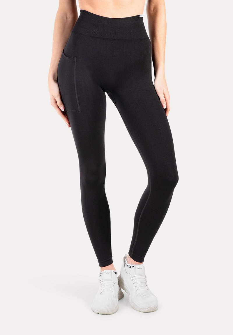 Hoge taille zwarte leggings van rekbaar materiaal, met een zijzak en platte naden voor comfort. Gemaakt om te dragen met witte sportschoenen.