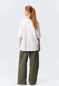 T-shirt bianco oversize con maniche corte e scollatura rotonda, abbinato a pantaloni larghi verde oliva con dettagli cuciti.